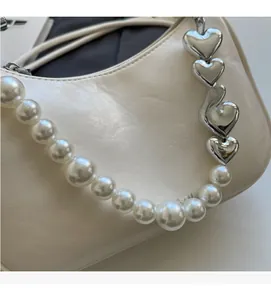 Close-up of white pleated leather bag with pearl and silver heart charm chain