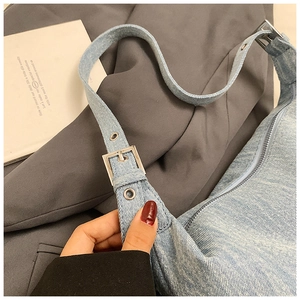 Detail of light blue denim shoulder bag featuring silver metal eyelets and zipper closure