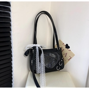 Detail of black patent leather bag featuring a heart-shaped window and white lace bow