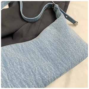 Close-up of light blue denim hobo bag with twill texture and silver metal buckle details