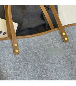 Close-up of light blue denim tote bag with brown leather straps and gold rivets