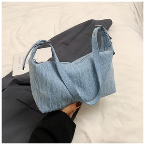 Detail of light blue denim hobo bag showing woven texture and adjustable silver eyelet strap