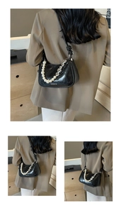 Detail of black faux leather baguette bag with pearl and silver heart chain strap