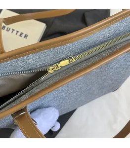 Close-up of smooth gold metal zipper and brown faux leather trim on gray canvas tote bag