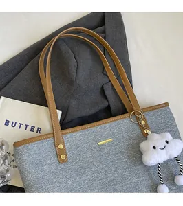 Detail of denim tote bag with brown leather straps and a white fluffy charm