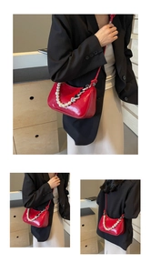 Detail of red glossy leather shoulder bag featuring heart charms and white pearl chain strap
