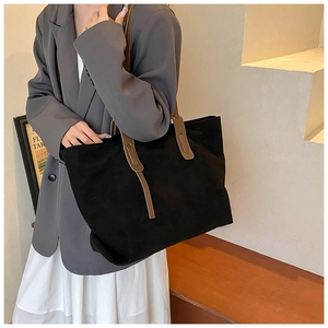 Detail of a large black suede tote bag with contrasting brown leather shoulder straps