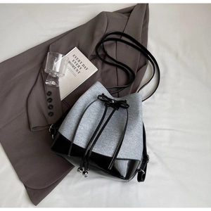 Detail of grey fabric and black patent leather contrast bucket bag with drawstring bow