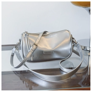 Detail of silver metallic cylinder bag featuring sleek brand plaque and smooth zipper
