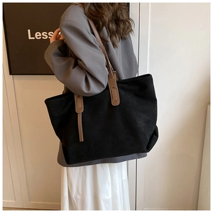 Detail of a large black suede tote bag with brown straps worn on a shoulder