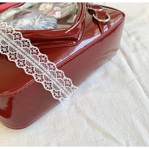 Detail of burgundy patent leather bag with heart window and white lace trim