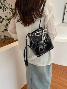 Glossy black leather backpack with pearl bow and silver chain straps on model