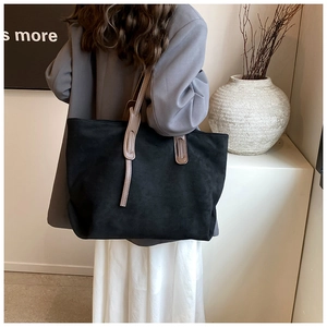 Detail of a black suede tote bag with brown straps worn by a model in a minimal suit