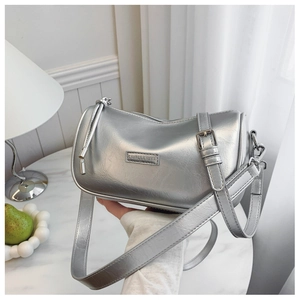 Detail of silver metallic cylinder bag with adjustable strap and brand metal plaque