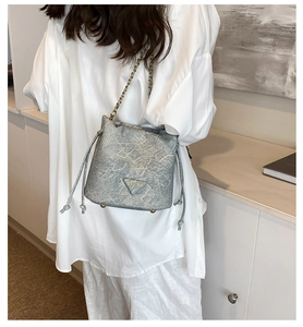 Close-up of light gray marble textured bucket bag with brass chain and metal logo