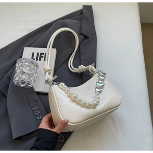 Detail of cream white faux leather bag with pearl chain and silver heart accents