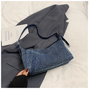 Close-up of blue denim texture shoulder bag with silver buckle on a gray blazer