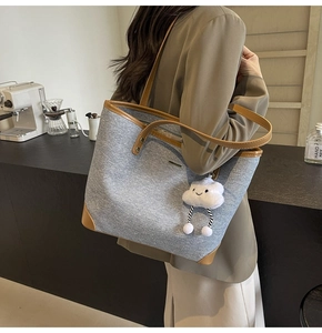 Detail view of denim tote bag with leather trim and white plush cloud charm accessory