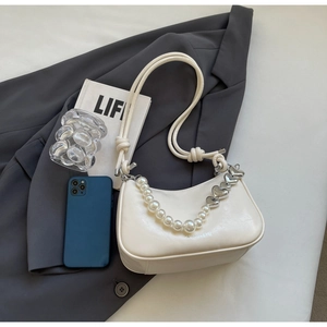 Detail of off-white leather shoulder bag with pearl heart chain next to a smartphone