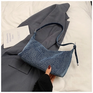 Close-up of blue denim shoulder bag with adjustable strap on a gray blazer and book