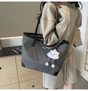 Detail of grey denim tote bag with black leather handles and white cloud plush charm