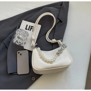 Detail of white crescent shoulder bag featuring pearl strap and silver heart pendant