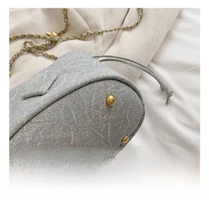 Close-up of grey bucket bag base with gold metal studs and woven chain strap details
