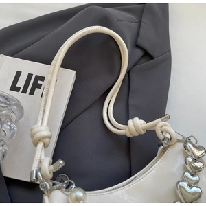 Close-up of beige crescent bag featuring silver heart chain and pearl charm detail