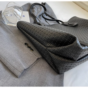 Detail of hand-woven black leather tote bag with Intrecciato texture and slim strap