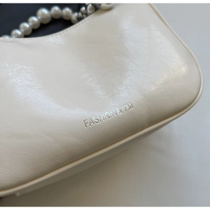 Detail view of cream white pleated leather texture with pearl handle and silver logo