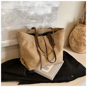 Detail of a khaki suede tote bag on a black blazer with fashion magazines and art props