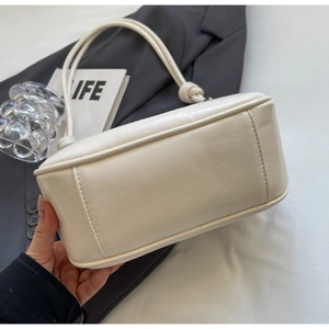 Close-up of cream white underarm bag featuring minimalist knotted strap and leather texture