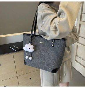 Detail of grey knit tote bag with black leather straps and a white cloud plush charm
