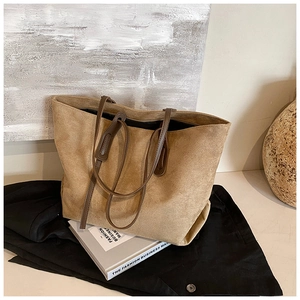 Detailed close-up of large khaki suede tote bag with brown straps in a minimalist setting