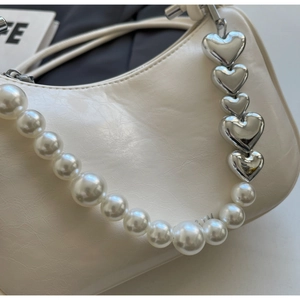 Detail of off-white leather shoulder bag with decorative pearl and silver heart chain