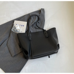 Detailed view of black woven faux leather tote bag placed on a grey blazer