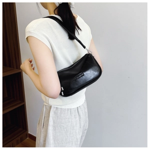 Side view of a minimalist black leather half-moon hobo bag worn on the shoulder