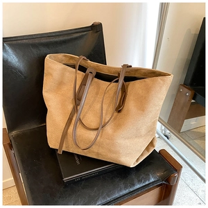 Detail of camel suede tote bag with brown leather handles on a leather chair