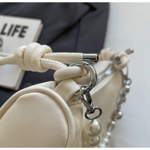 Detail of cream pleated shoulder bag with silver hardware and pearl strap embellishment