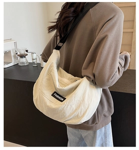 Close-up of beige canvas crescent bag with fashion tag on model in a cozy cafe