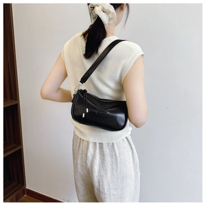 Detail of a black glossy underarm bag featuring a slim shoulder strap and silver hardware