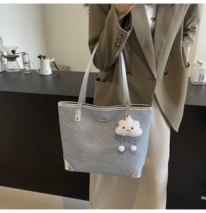 Close-up of grey texture denim tote bag featuring silver straps and plush cloud charm