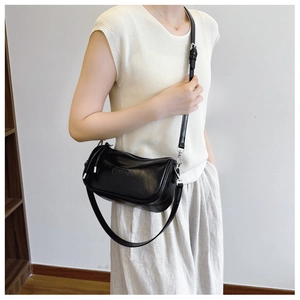 Close-up of a black pillow bag with smooth leather texture on a white knit outfit
