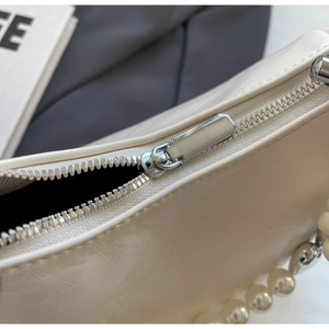 Detail of silver zipper closure and large pearl strap on cream pleated leather handbag