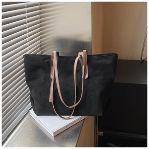 Detail view of large black suede tote bag with contrast slim leather straps on book