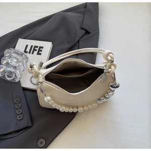 Detail of cream shoulder bag featuring pearl chain, silver heart charm and knotted strap