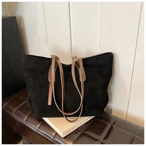 Detail of black suede tote bag with brown handles resting on a leather cushion