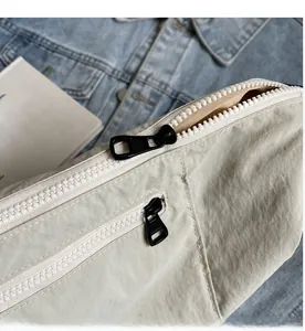 Close-up of white nylon crossbody bag with smooth dual zipper details and metal pullers