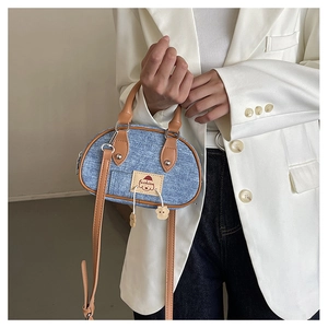 Dettaglio della mini borsa in denim a contrasto con manici in pelle marrone e charm