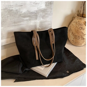 Detail of black suede tote bag featuring brown straps and minimalist texture in a home setting